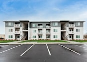 Thumbnail 10 of 34 - Apartment building with a parking lot in front.