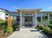 Thumbnail 29 of 34 - A white building with a glass door and windows is surrounded by plants.