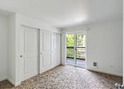 Thumbnail 15 of 29 - A room with white walls and a carpeted floor with a sliding glass door leading to a balcony.
