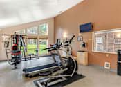 Thumbnail 28 of 29 - A gym with treadmills, elliptical machines, and a television.