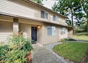 Thumbnail 25 of 29 - A house with a brown siding and a black door is surrounded by greenery.