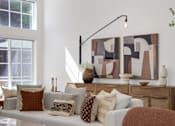 Thumbnail 23 of 38 - A living room with a couch, pillows, and a large abstract painting on the wall.
