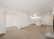 Thumbnail 6 of 16 - A white room with a carpet floor and a kitchen area in the background.