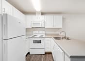 Thumbnail 8 of 16 - A white kitchen with a refrigerator, microwave, oven, and sink.