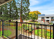 Thumbnail 49 of 49 - A balcony with a black railing overlooks a garden with a tree and a house in the background.