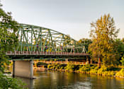 Thumbnail 8 of 8 - A green bridge over a river with trees on the left.