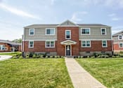 Thumbnail 1 of 36 - A brick building with a front yard and a walkway leading to the front door.