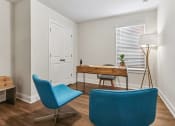 Thumbnail 26 of 31 - a living room with two blue chairs and a desk and a window