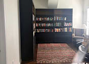Thumbnail 14 of 15 - A room with a bookshelf filled with books and a rug on the floor.
