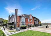 Thumbnail 9 of 26 - A large brick building with a black fence in front.