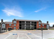 Thumbnail 7 of 26 - A large brick building with a parking lot in front.