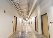 Thumbnail 10 of 16 - A long hallway with doors on both sides and a fire extinguisher on the wall.