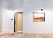 Thumbnail 13 of 16 - A painting hangs on the wall in a room with a wooden door.