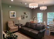 Thumbnail 7 of 11 - A living room with a brown leather couch, a striped armchair, and a small table with a lamp.