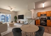 Thumbnail 11 of 23 - A modern living room with a flat screen TV, a kitchen area, and a dining table.