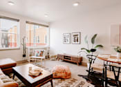 Thumbnail 2 of 22 - A living room with a brown leather couch, a wooden coffee table, and a large window with a view of a building outside.