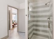 Thumbnail 6 of 22 - A bathroom with a walk-in shower and a doorway leading to a living room.