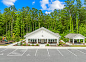 Thumbnail 1 of 6 - A white building with a parking lot in front of it.