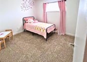 Thumbnail 11 of 17 - A pink bed with a teddy bear on it sits in a room with a carpeted floor.