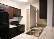 Thumbnail 6 of 10 - A kitchen with a black refrigerator and a stove top oven.