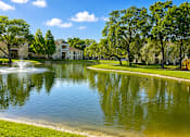 Thumbnail 7 of 15 - A serene lake in a park with a building in the background.