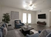 Thumbnail 14 of 33 - A living room with a grey couch, a blue chair, a coffee table, and a flat screen TV mounted on the wall.