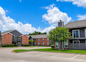 Thumbnail 24 of 27 - A parking lot in front of a brick apartment building.