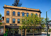 Thumbnail 7 of 7 - A large building with a black awning sits on a street corner.