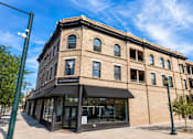 Thumbnail 3 of 7 - A large building with a black awning sits on a street corner.