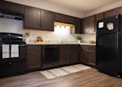 Thumbnail 3 of 14 - A black refrigerator stands in a kitchen with brown cabinets and a white backsplash.