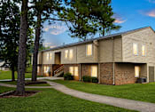 Thumbnail 3 of 4 - A building with a brown siding and a brick wall is surrounded by a grassy area and trees.