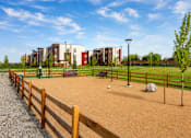 Thumbnail 25 of 25 - A playground with a wooden fence and a building in the background.