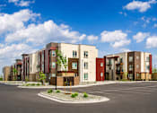 Thumbnail 6 of 25 - A row of modern apartment buildings with a parking lot in front.