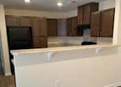 Thumbnail 3 of 6 - A kitchen with brown cabinets and a black fridge.