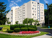 Thumbnail 1 of 12 - A large white building with a flower bed in front.