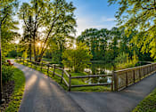 Thumbnail 4 of 12 - A paved road leads to a wooden bridge over a body of water.