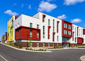 Thumbnail 2 of 25 - A modern building with a red and white facade and a yellow mural on the side.