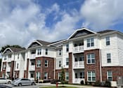 Thumbnail 1 of 9 - a brick and white apartment building with cars parked in front