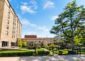 Thumbnail 2 of 16 - A large building with a red roof is surrounded by a black fence and a large tree.