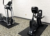 Thumbnail 15 of 16 - Two exercise bikes are placed on mats in a room with a white brick wall.