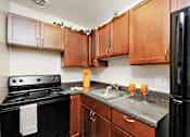 Thumbnail 6 of 15 - A kitchen with black appliances and wooden cabinets.