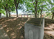 Thumbnail 2 of 15 - A monument with a plaque on it is surrounded by trees.