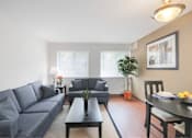 Thumbnail 7 of 15 - A living room with a grey couch, a black coffee table, and a dining table with chairs.