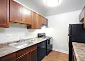 Thumbnail 8 of 15 - A kitchen with brown cabinets and a black fridge.