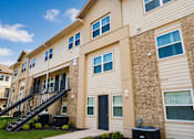 Thumbnail 2 of 5 - A beige apartment building with a black door and a black staircase.