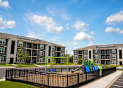 Thumbnail 13 of 22 - A playground with a slide is in front of apartment buildings.
