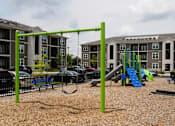 Thumbnail 11 of 22 - A playground with a green swing set and a blue slide.