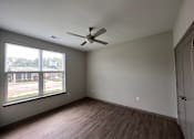 Thumbnail 22 of 22 - A room with a ceiling fan and a window overlooking a parking lot.