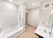 Thumbnail 19 of 22 - A white bathroom with a wooden floor and a white tub.