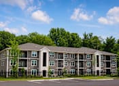 Thumbnail 6 of 22 - A large apartment building with a black fence in front.